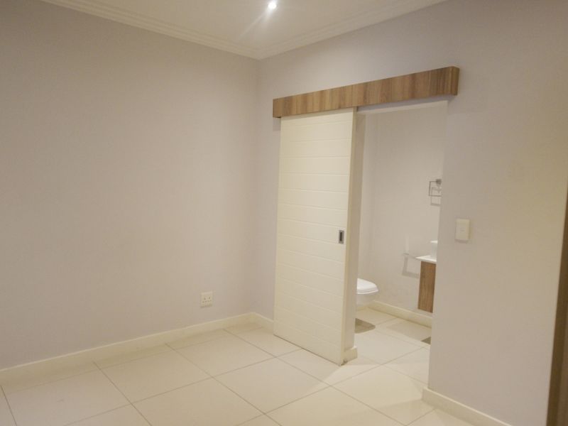 A clean, empty bedroom featuring neutral tiled flooring, recessed lighting, and a modern sliding door leading to an en-suite bathroom.