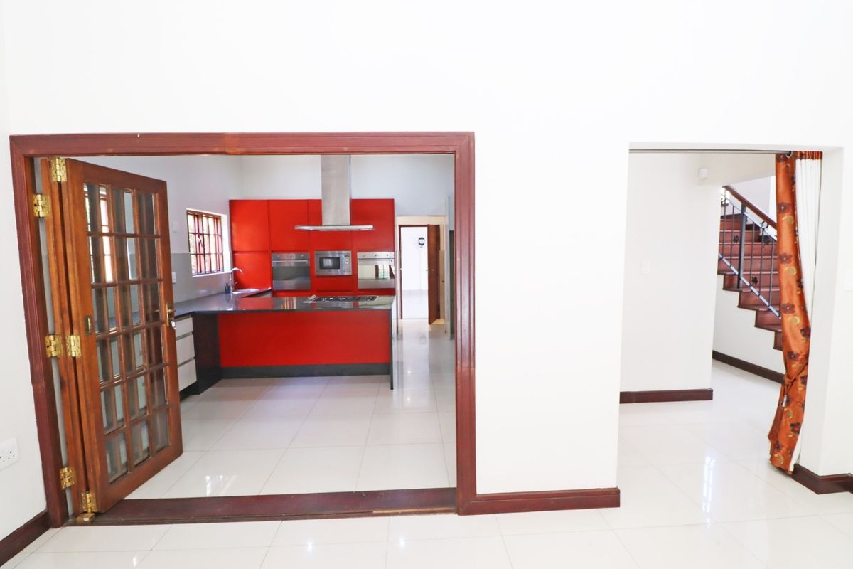 A view into a kitchen featuring bold red cabinetry, built-in appliances, and tiled flooring, with an adjacent staircase visible in the hallway.