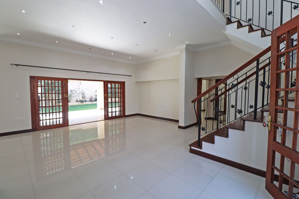 Spacious, light-filled living area featuring polished porcelain tiles, recessed lighting, and a feature wooden staircase with wrought iron detailing, opening onto the garden.