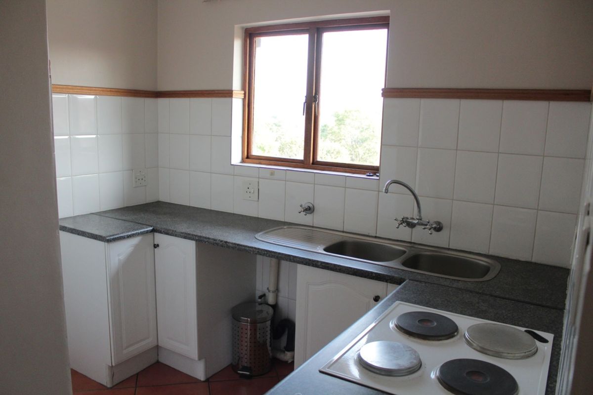 A functional kitchen featuring white cabinetry, laminate countertops, a double bowl sink, and an integrated electric hob with tiled splashbacks.