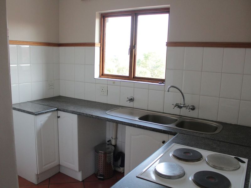 A functional kitchen featuring white cabinetry, laminate countertops, a double bowl sink, and an integrated electric hob with tiled splashbacks.