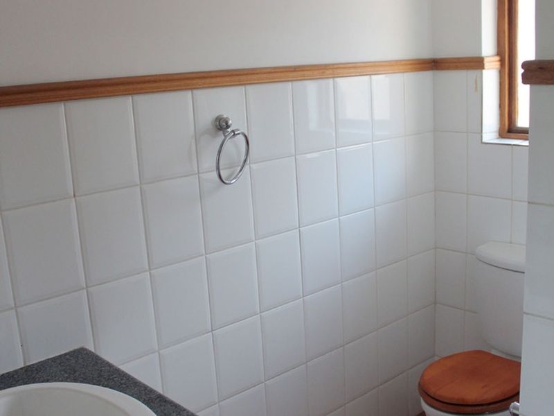 A functional bathroom featuring a vanity with a granite countertop, white wall tiling, and terracotta floor tiles.