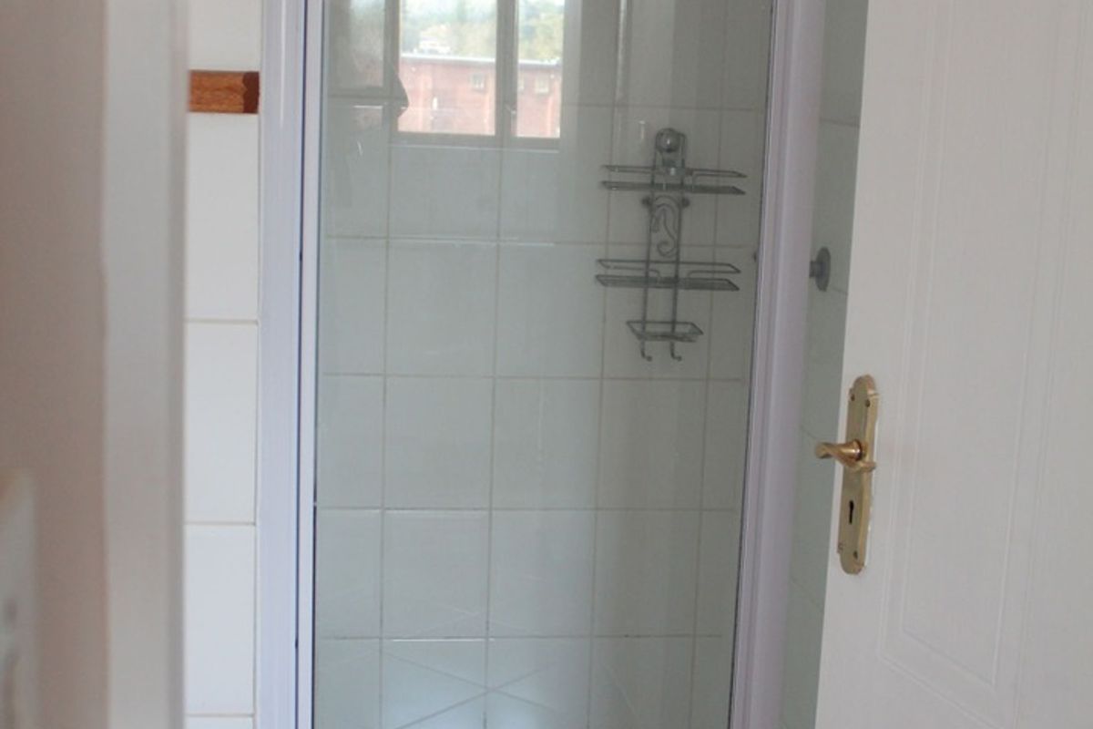 A compact bathroom shower enclosure featuring white wall tiles and a standard shower fixture.