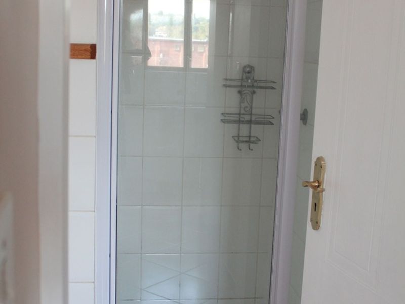 A compact bathroom shower enclosure featuring white wall tiles and a standard shower fixture.