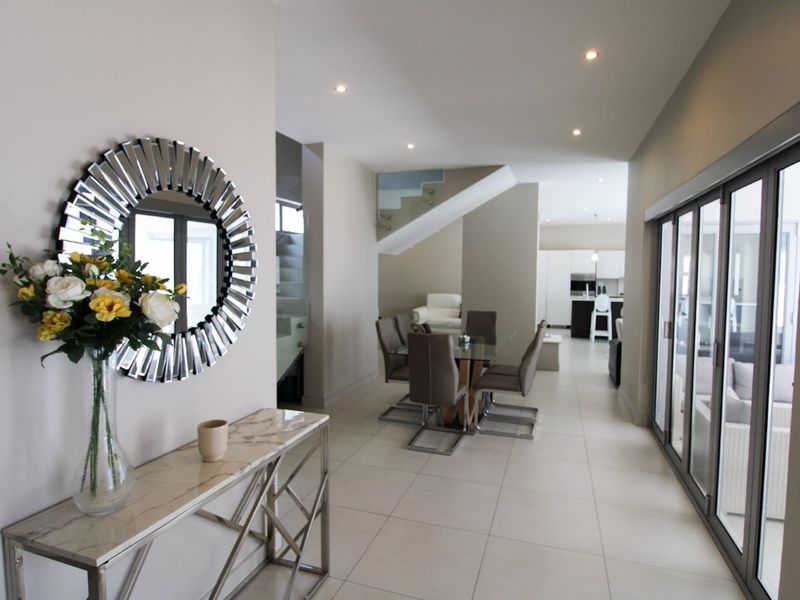 Spacious open-plan living area featuring modern tiled flooring, recessed downlights, and a contemporary staircase with a glass balustrade leading to the upper level.