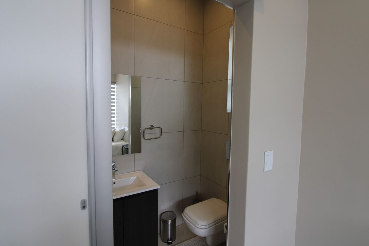 A compact, modern guest bathroom featuring neutral wall tiles, a vanity basin, and a wall-mounted toilet.