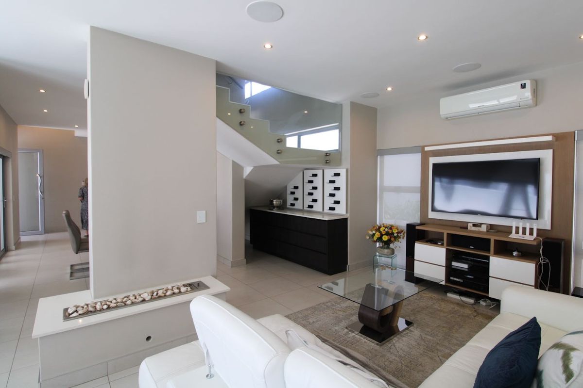 Modern living room featuring a built-in fireplace, glass balustrade staircase, recessed lighting, and split-system air conditioning with neutral tiled flooring.