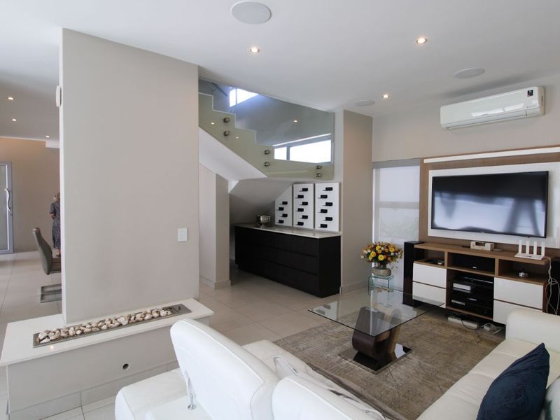 Modern living room featuring a built-in fireplace, glass balustrade staircase, recessed lighting, and split-system air conditioning with neutral tiled flooring.