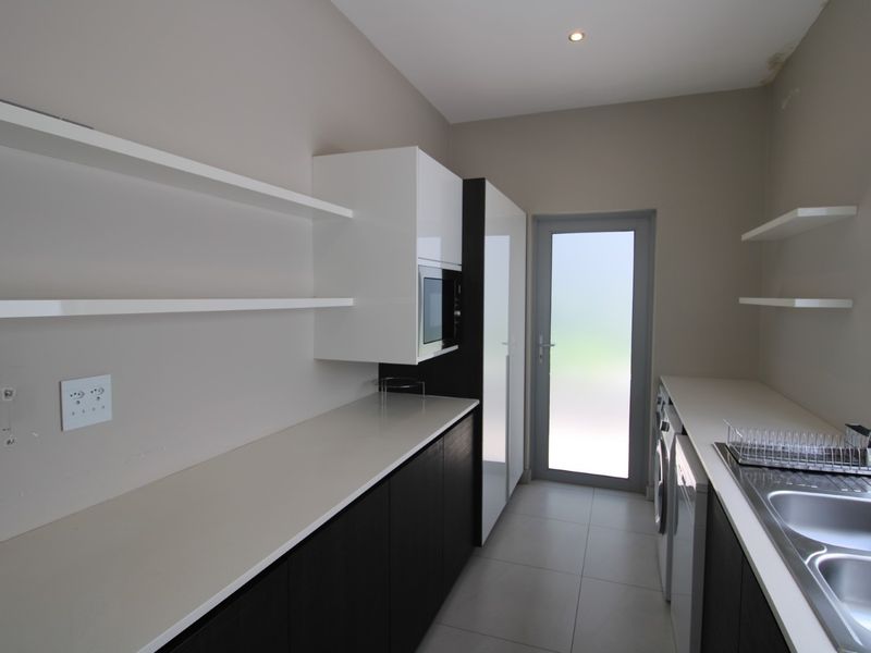 Modern scullery featuring sleek dark and white cabinetry, stone countertops, double sink, and direct access to the exterior via a frosted glass door.