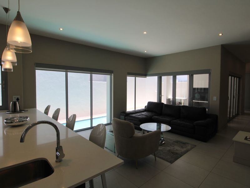 Modern open-plan living area featuring a sleek kitchen island, tiled floors, and large sliding doors providing seamless access to the outdoor pool area.