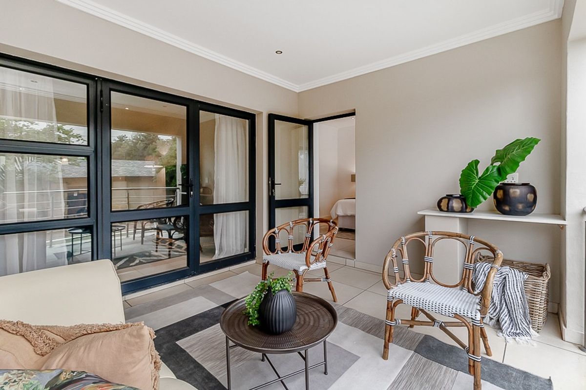 A covered balcony featuring tiled flooring, modern black aluminium framed glass doors, and recessed ceiling lighting, providing a seamless transition to the interior living space.
