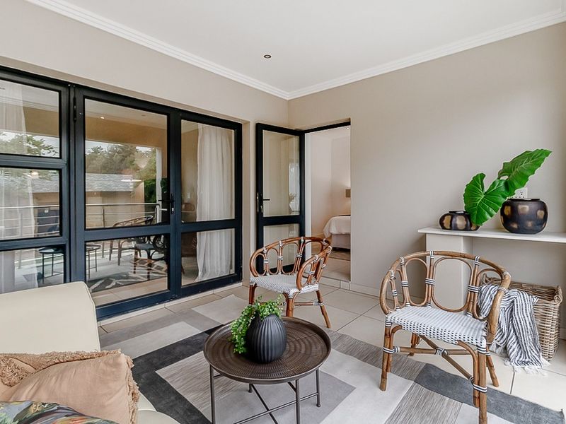 A covered balcony featuring tiled flooring, modern black aluminium framed glass doors, and recessed ceiling lighting, providing a seamless transition to the interior living space.