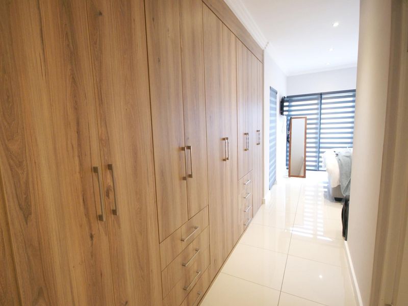 Modern bedroom featuring extensive floor-to-ceiling wood-finish built-in cupboards, polished tile flooring, and access to a balcony through sliding doors.