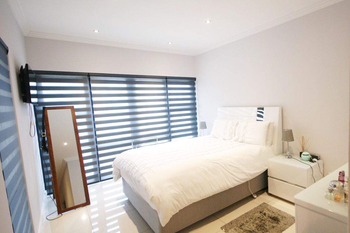 A well-maintained bedroom featuring tiled flooring, recessed downlighting, and modern roller blinds, offering a clean and neutral living space.