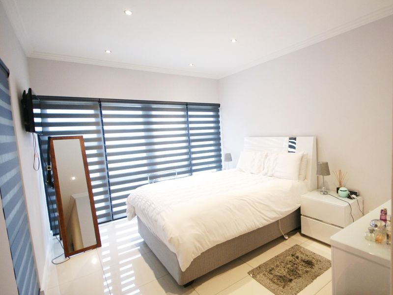 A well-maintained bedroom featuring tiled flooring, recessed downlighting, and modern roller blinds, offering a clean and neutral living space.