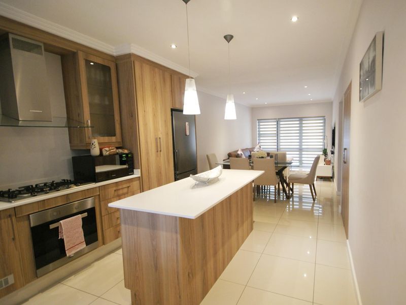 Modern open-plan kitchen and dining area featuring wood-finish cabinetry, a central island with stone countertop, and sleek tiled flooring throughout.