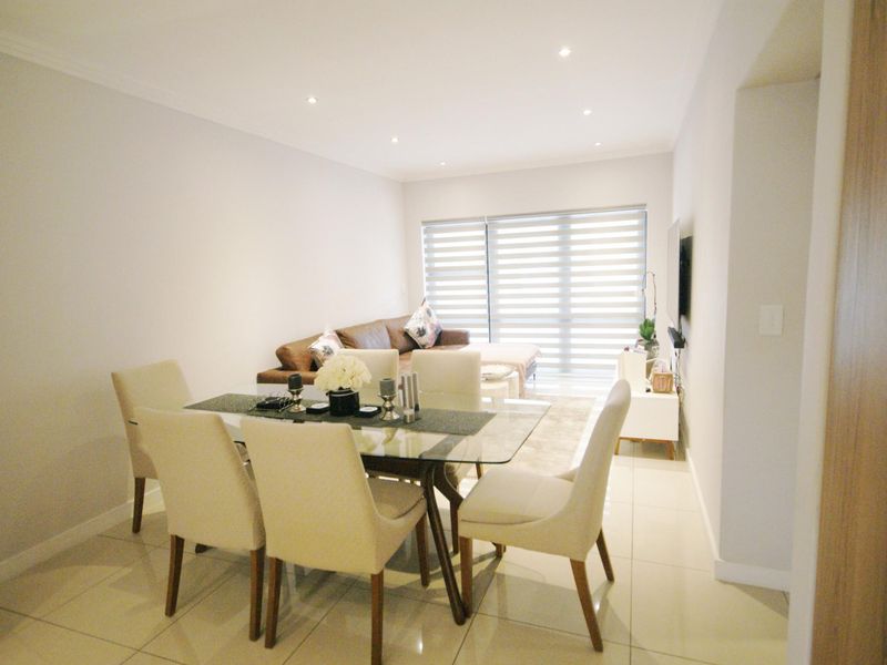 A bright open-plan living and dining area featuring modern tiled flooring, recessed downlighting, and large sliding glass doors with roller blinds.