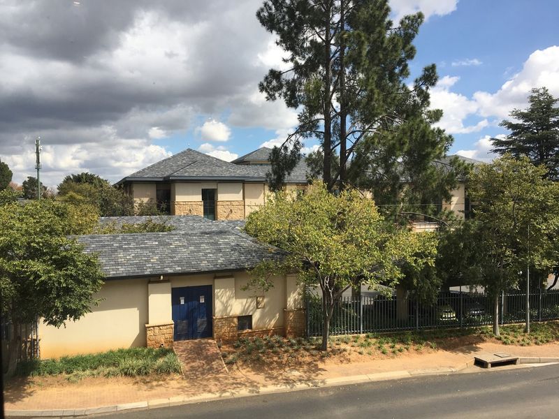 Front exterior view of the apartment complex featuring stone cladding, tiled roofing, and secure perimeter fencing with a paved entrance walkway.