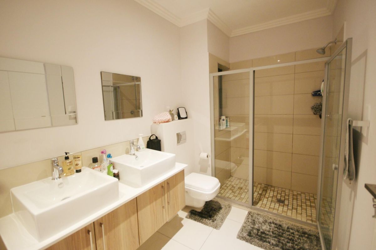 Modern bathroom featuring a double vanity with vessel sinks, a wall-mounted toilet, and a spacious walk-in shower with a glass enclosure.
