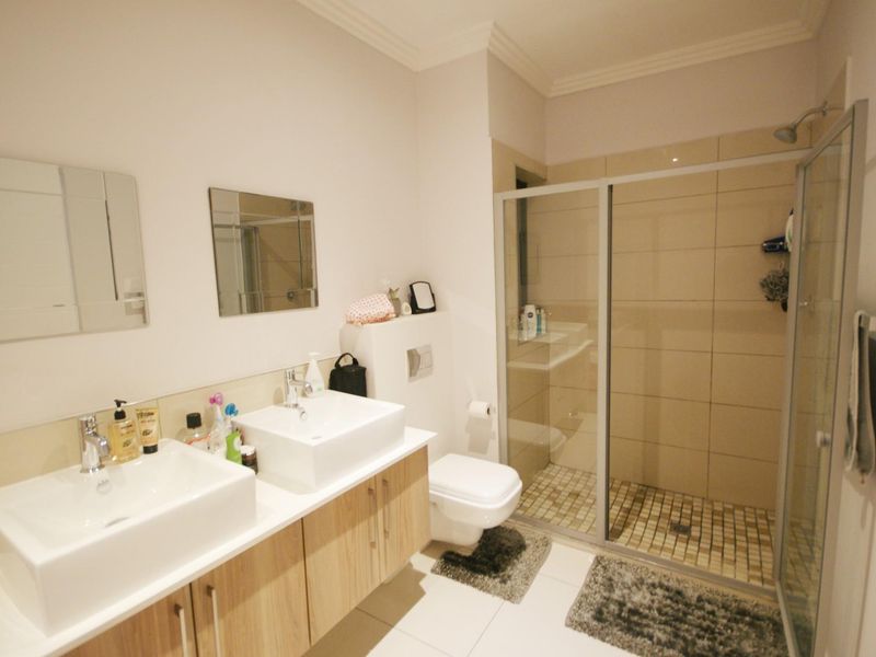 Modern bathroom featuring a double vanity with vessel sinks, a wall-mounted toilet, and a spacious walk-in shower with a glass enclosure.
