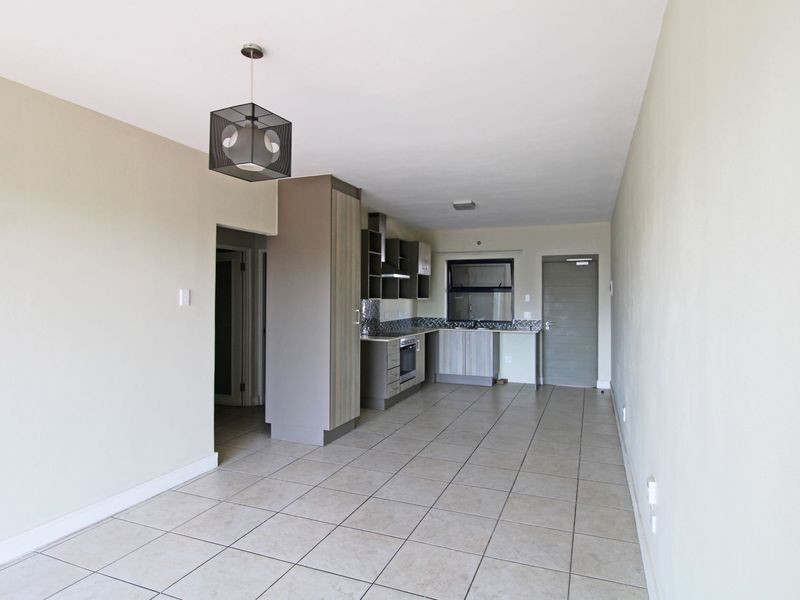 An open-plan living and kitchen area featuring tiled flooring, modern built-in cabinetry, and integrated kitchen appliances.