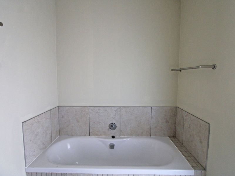 A clean, empty bathroom featuring a built-in bathtub with neutral tiled splashback and chrome fixtures.