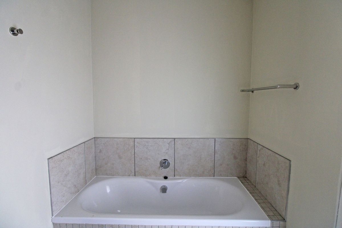 A clean, empty bathroom featuring a built-in bathtub with neutral tiled splashback and chrome fixtures.