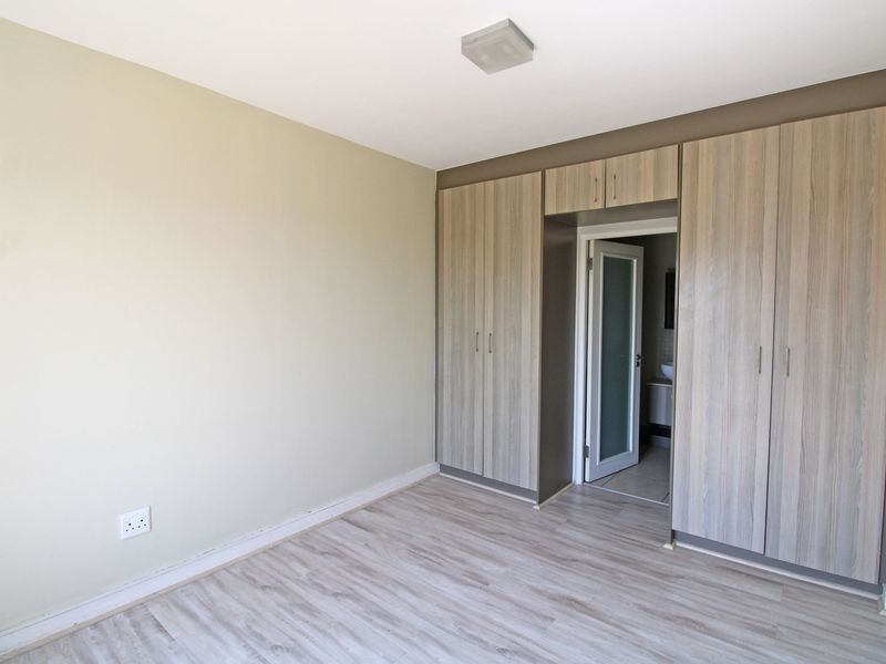 A clean, empty bedroom featuring modern wood-look laminate flooring and extensive built-in cupboards with a neutral color palette.