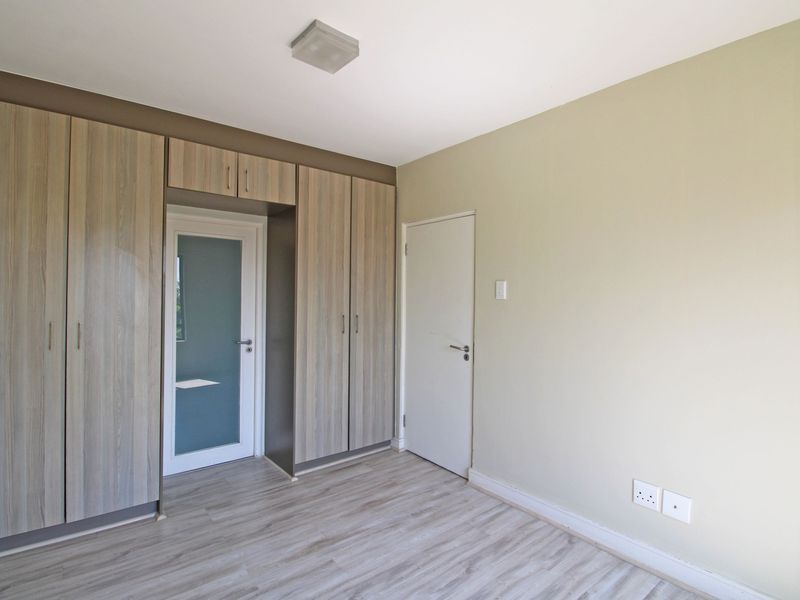 A clean, empty bedroom featuring modern wood-look laminate flooring, ample built-in cupboard storage, and a frosted glass door leading to an adjacent space.