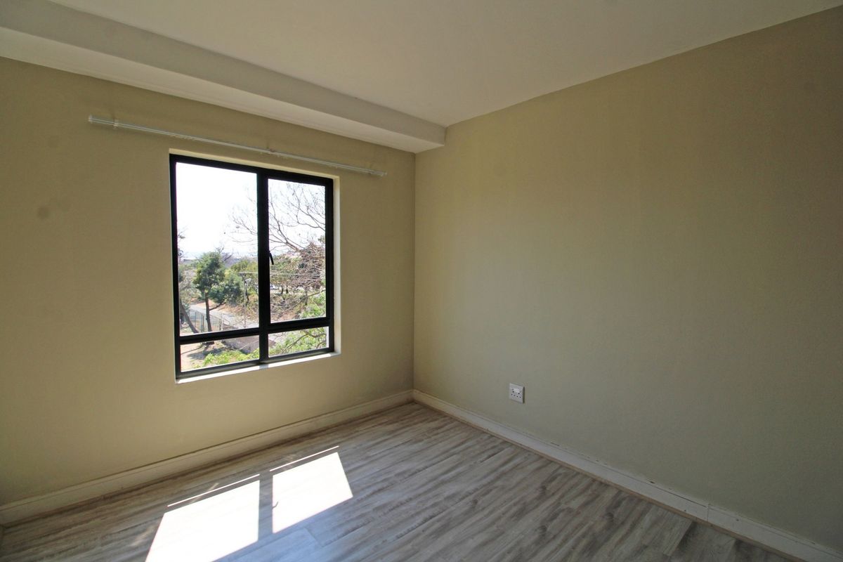 A bright, empty bedroom featuring light-toned laminate flooring, neutral wall paint, and an aluminium-framed window with a curtain rod.