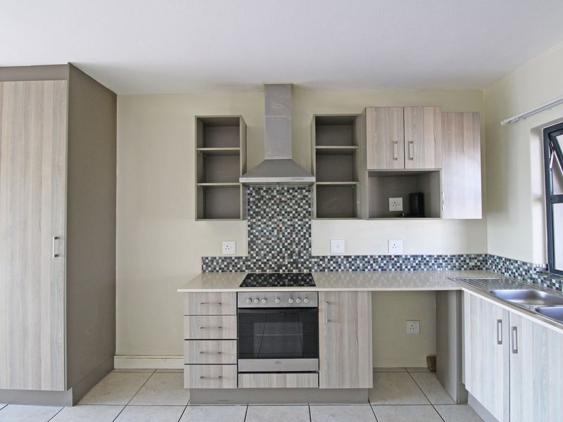 Modern kitchen featuring light wood-grain cabinetry, stone countertops, mosaic tile splashback, and integrated stainless steel appliances including an oven and hob.