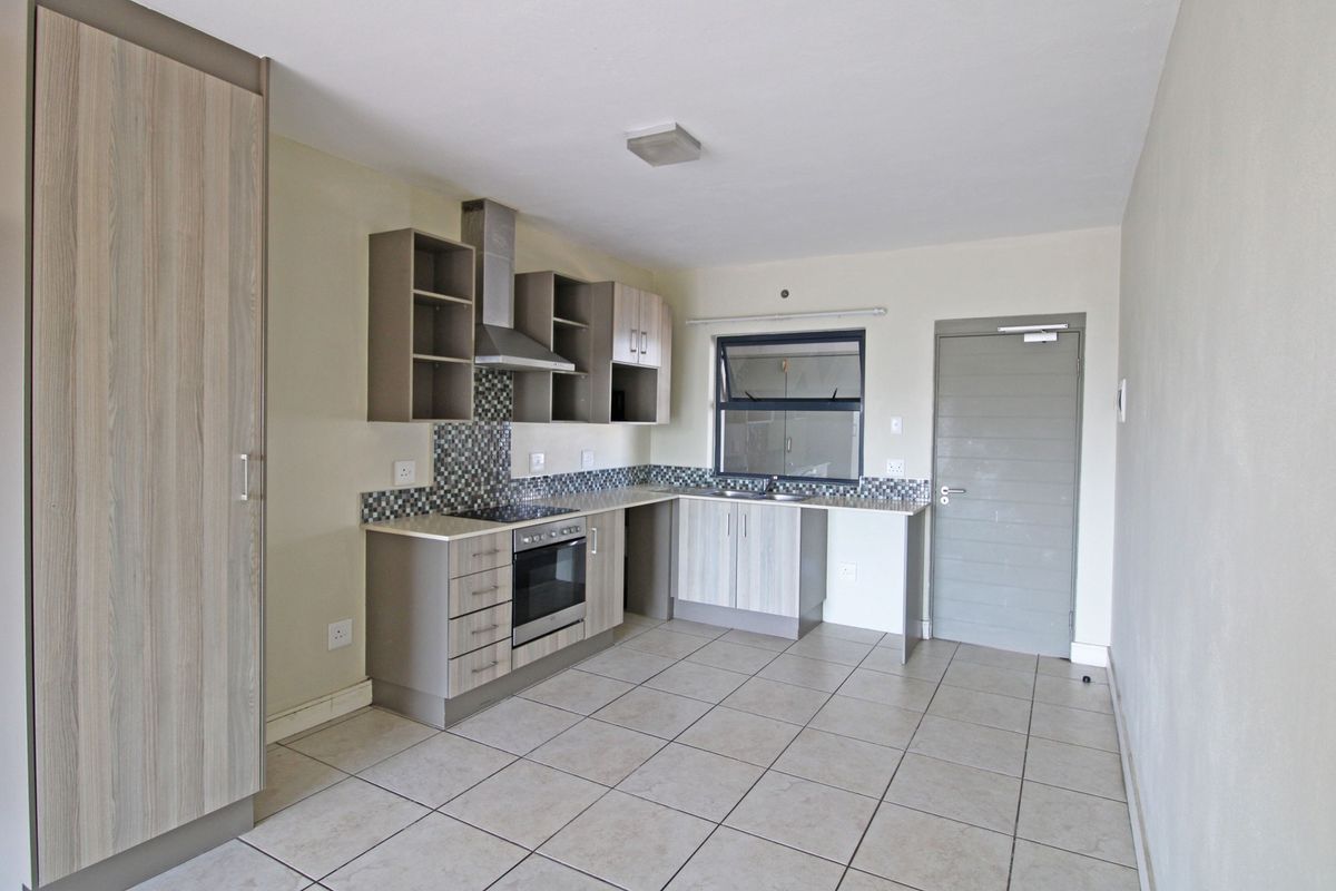 Modern kitchen featuring light wood-grain cabinetry, mosaic tile backsplash, built-in oven and hob, and neutral tiled flooring in an open-plan layout.