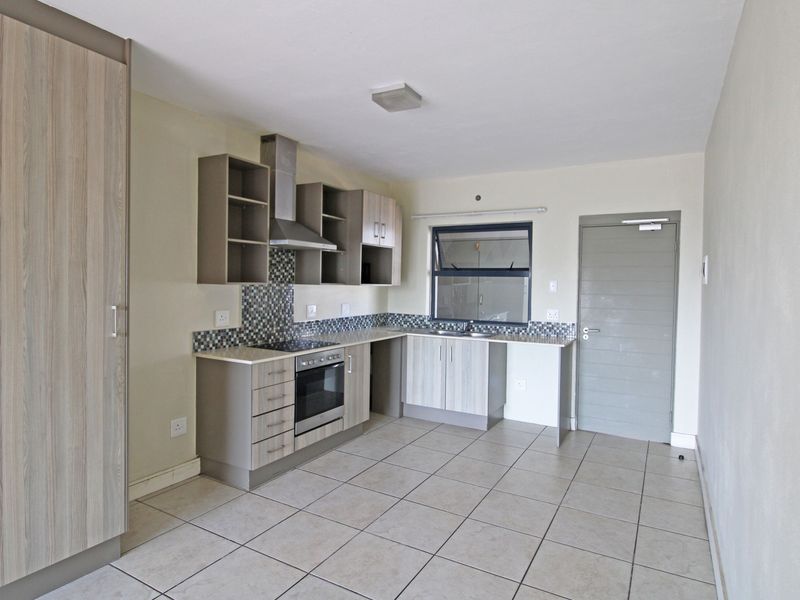 Modern kitchen featuring light wood-grain cabinetry, mosaic tile backsplash, built-in oven and hob, and neutral tiled flooring in an open-plan layout.