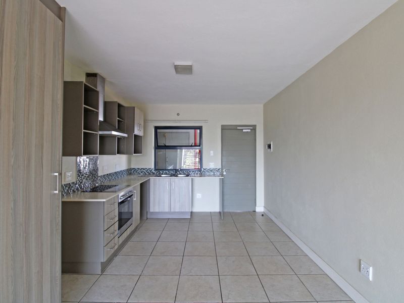 Open-plan kitchen and living area featuring tiled flooring, modern cabinetry, built-in oven, hob, and a mosaic tile backsplash.