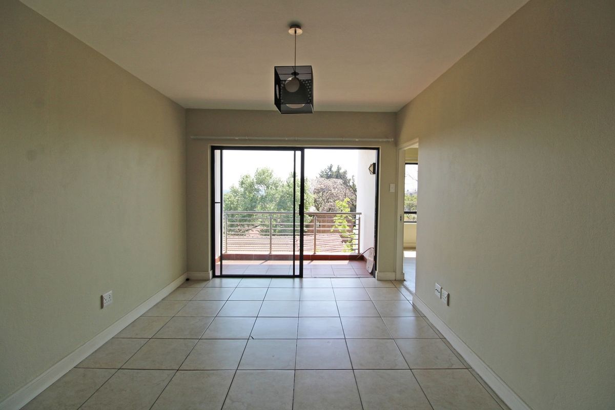 An empty living room featuring neutral tiled flooring, a central pendant light, and a sliding glass door leading to an outdoor balcony.