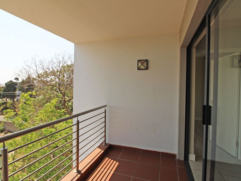 A clean, covered balcony featuring tiled flooring, a stainless steel balustrade, and sliding glass door access to the interior.