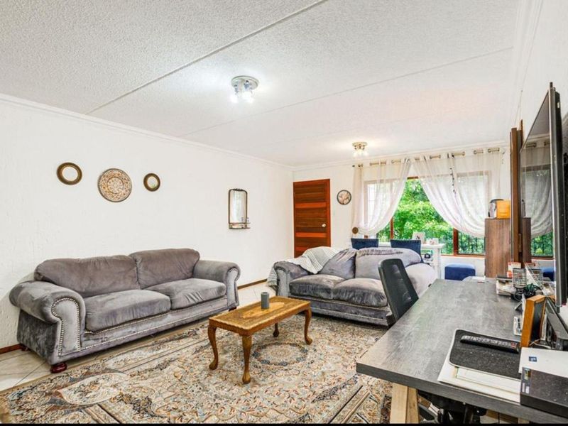 A spacious living room featuring tiled flooring, textured ceilings, and natural light from a large window, providing a comfortable and functional living area.