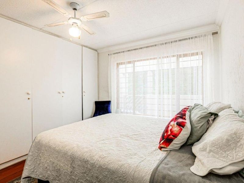 A bedroom featuring built-in cupboards, a ceiling fan, and large windows with security bars, providing natural light and functional storage space.