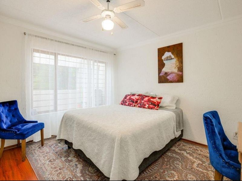 A well-lit bedroom featuring a ceiling fan, large window with natural light, and textured wall finishes.