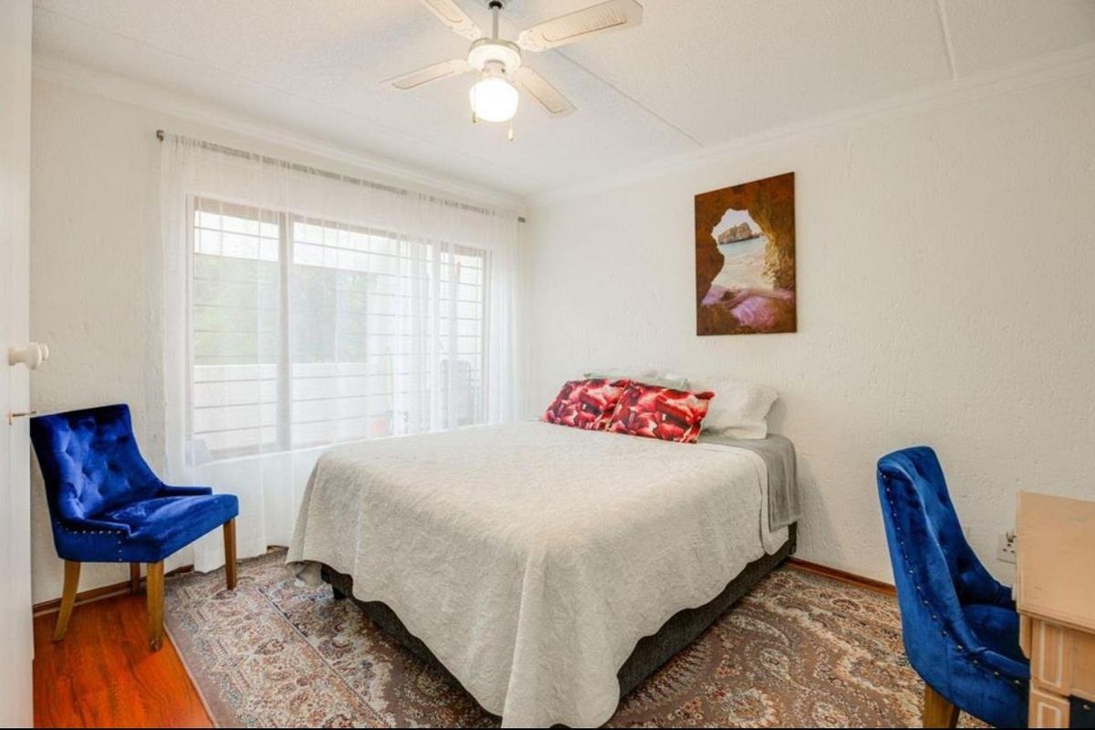 A well-lit bedroom featuring a ceiling fan, large window with natural light, and textured wall finishes.