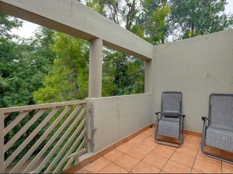 A private balcony featuring tiled flooring, a concrete balustrade, and metal railings, offering an outdoor space with views of surrounding trees.