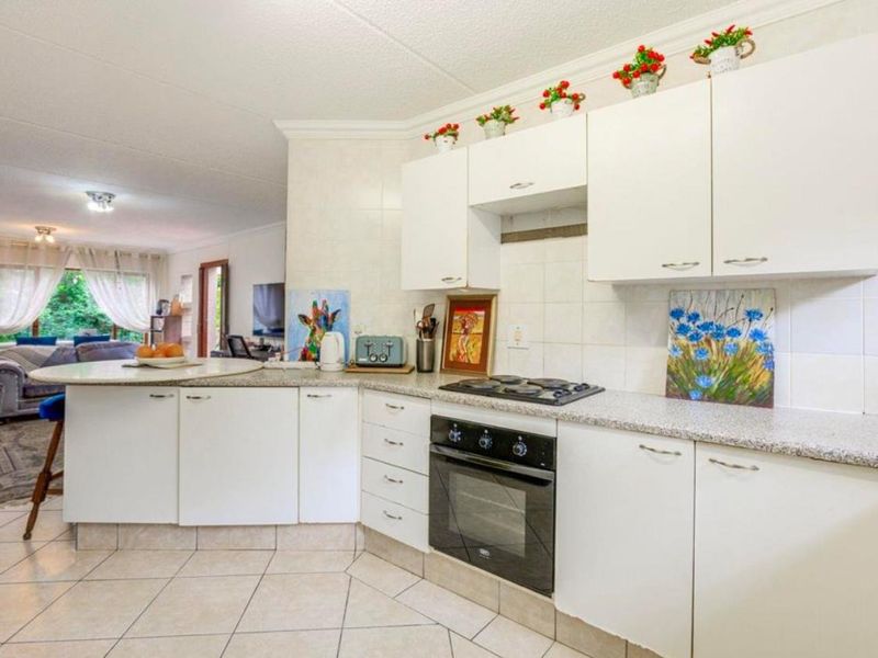 Open-plan kitchen featuring white cabinetry, laminate countertops, built-in oven and hob, flowing into a bright living area with tiled flooring throughout.