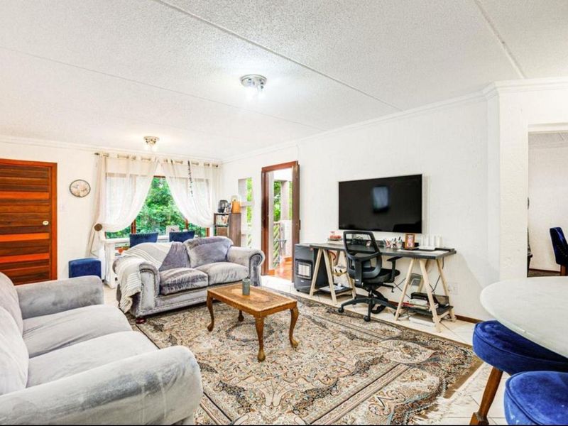 A spacious living room featuring tiled flooring, textured ceilings, and direct access to an outdoor area through a sliding door.