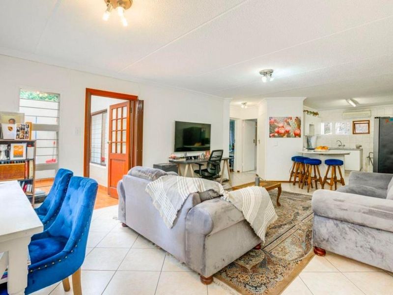 Open plan living and kitchen area featuring tiled flooring, a breakfast bar, and direct access to an adjacent room through a timber door frame.