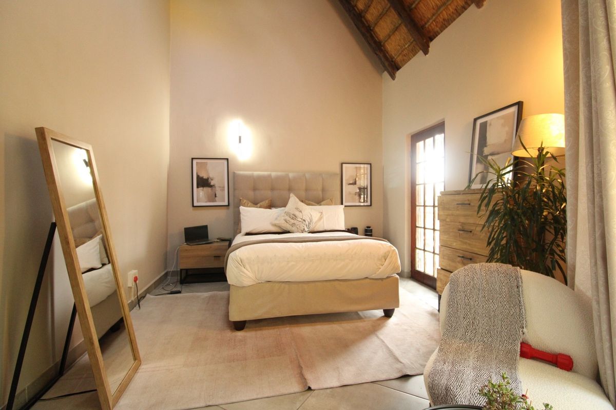 A well-lit bedroom featuring a high vaulted thatched ceiling, tiled flooring, and a glass panel door providing natural light.