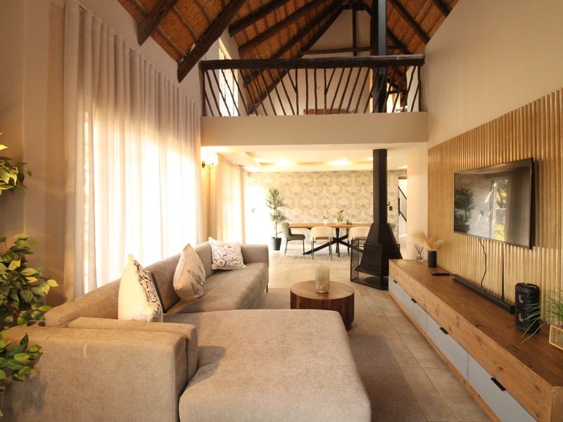 Spacious open-plan living area featuring a high vaulted thatch ceiling with exposed beams, a mezzanine level, and a modern timber slat feature wall.