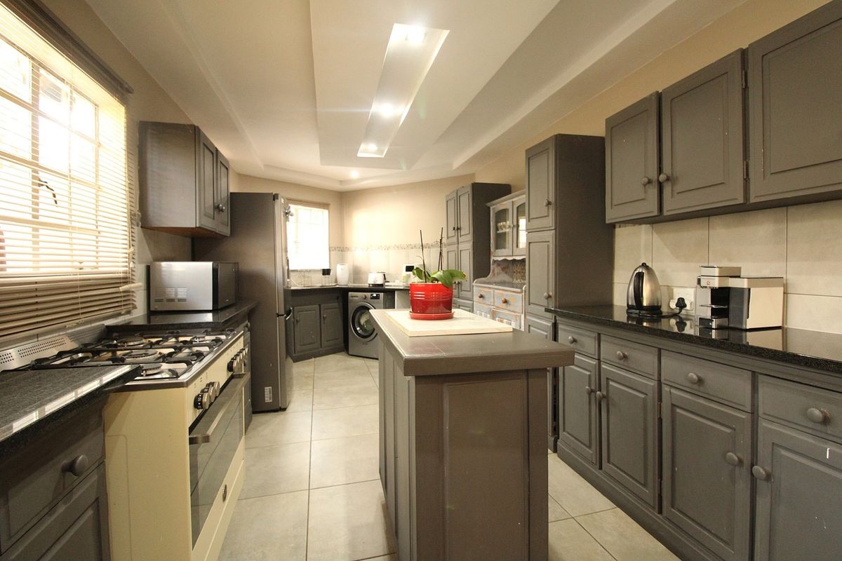 A well-appointed kitchen featuring dark grey cabinetry, granite countertops, a central island, gas stove, and modern recessed ceiling lighting.