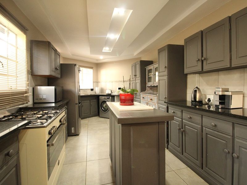 A well-appointed kitchen featuring dark grey cabinetry, granite countertops, a central island, gas stove, and modern recessed ceiling lighting.