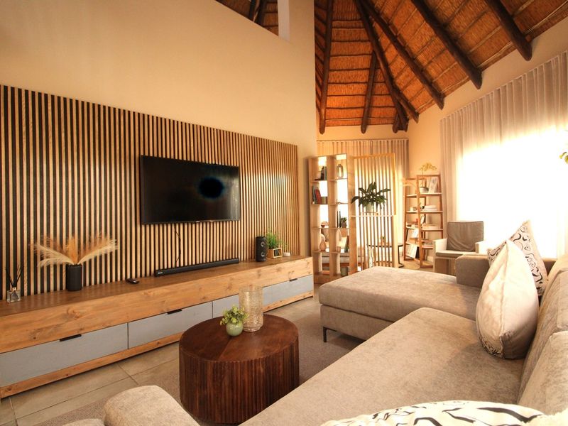 Spacious living room featuring a high thatched ceiling with exposed rafters, a modern timber slat feature wall, and a built-in media console.