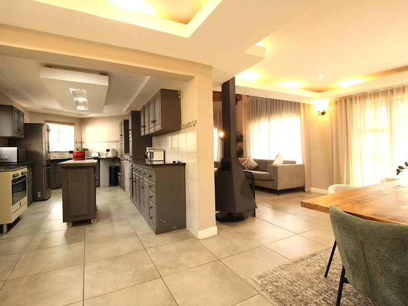 Spacious open-plan living area featuring a modern kitchen with island, tiled flooring, recessed lighting, and a striking central fireplace connecting to the dining space.